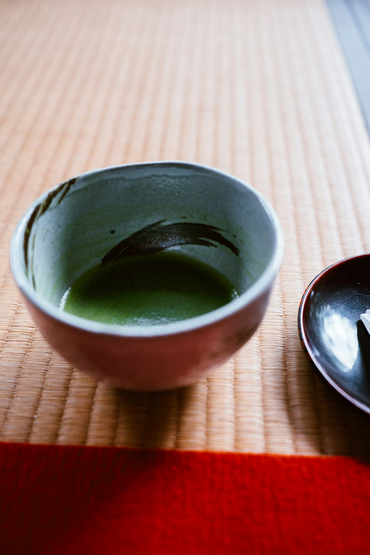Matcha-Schale mit leuchtendem Grüntee und Bambus-Chasen auf Holzunterlage