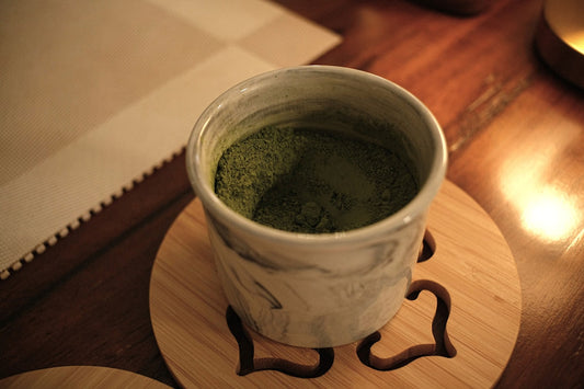 Tasse Matcha-Tee auf einem Untersetzer im warmen Abendlicht auf einem Holztisch
